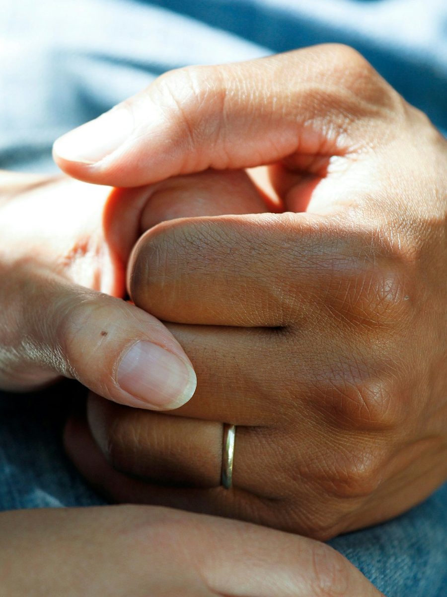 Two hands held gently together, one supporting the other, resting on a bed